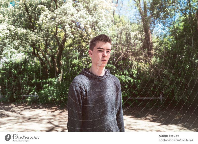 Porträt eines ernsthaften jungen Mannes in einem Park cool lässig Sonnenlicht Sonnenstrahlen im Freien Perspektive trendy selbstbewusst Teenager Blick männlich