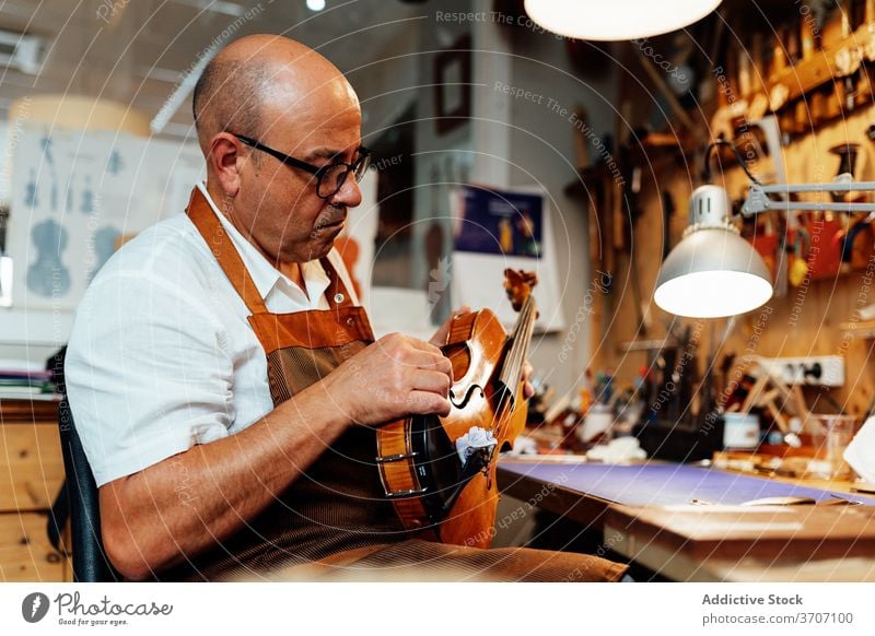 Handwerker mit Geige in professioneller Werkstatt Kunsthandwerker Reparatur Zupfinstrumentenmacher Kunstgewerbler Arbeit Mann wiederherstellen Meister Fähigkeit