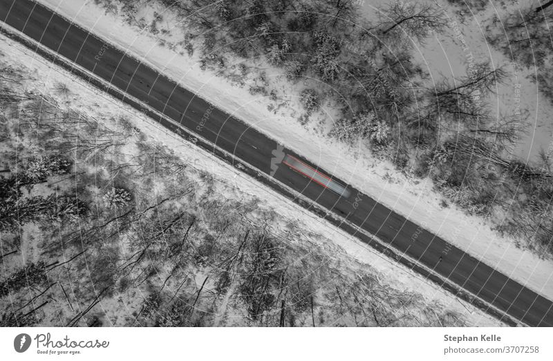 Luftaufnahme einer von Schnee umrahmten Winterstraße, ein Auto fährt als Langzeitbelichtung vorbei. Straße PKW diagonal Linie Lichter schwaebische Alb albstadt