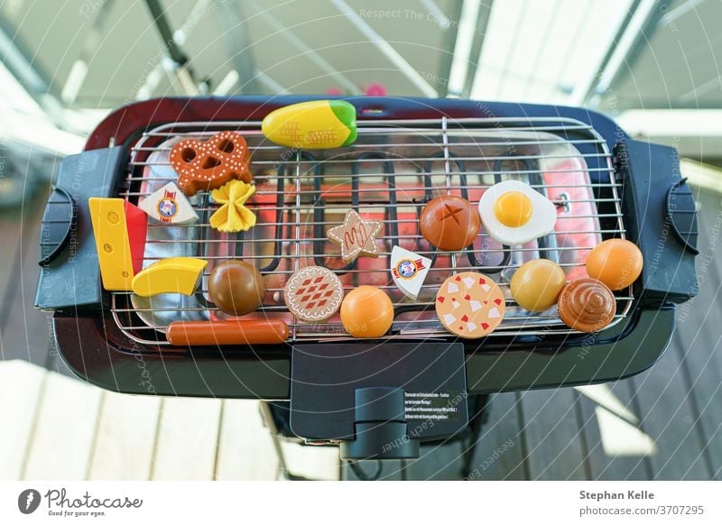 Ein elektronischer Grill auf dem Balkon voll reserviert mit Spielzeuggemüse und Würstchen Grillrost Lebensmittel heimwärts Braten Sommer Rippen grillen