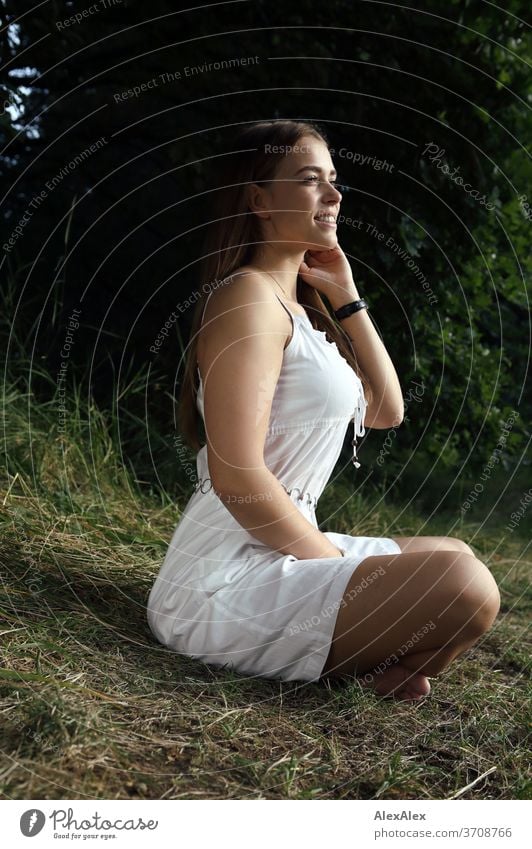 Portrait einer jungen Frau in weißem Sommerkleid im Schneidersitz in der Natur Licht sportlich feminin Gefühle emotional Blick in die Kamera Porträt