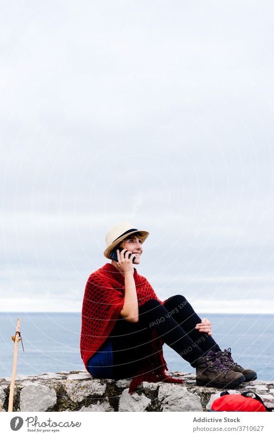 Weibliche Wanderer mit Smartphone während der Rast in der Nähe von Meer Reisender Frau benutzend Pilgerfahrt Wanderung Rucksack Seeküste Browsen