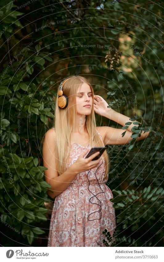 Ruhige junge Frau beim Musikhören im Garten zuhören Smartphone Kopfhörer Gelassenheit sich[Akk] entspannen Windstille genießen blond Technik & Technologie