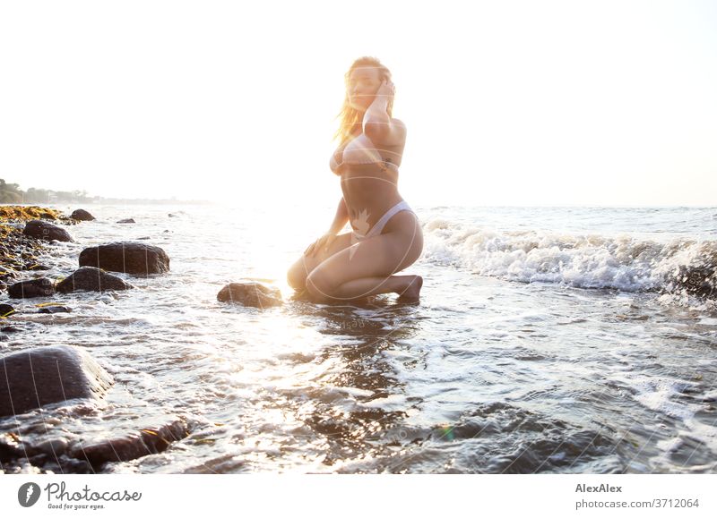 Portrait einer jungen, blonden Frau im Bikini, die in der Ostsee- Brandung kniet junge Frau Mädchen 18-20 Jahre schlank schön lockig sinnlich natürlich