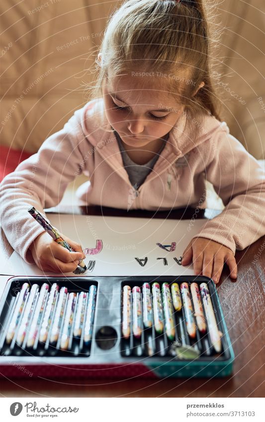 Kleines Mädchen im Vorschulalter, das zu Hause lernt, Briefe zu schreiben. Kind benutzt Buntstifte bei Hausaufgaben. Konzept der Früherziehung Aufmerksamkeit