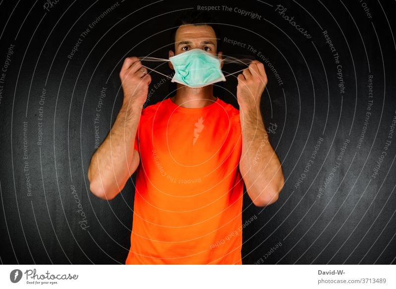 Mann hält sich eine Maske / Munschutz vor das Gesicht Corona Hände festhalten aufziehen anziehen aufsetzen testen Maskenpflicht Menschen coronavirus Coronavirus