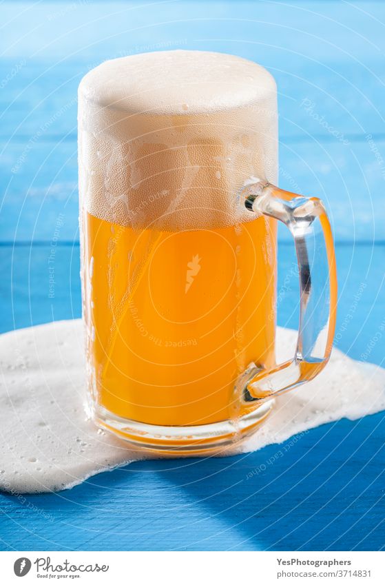 Ein Pint Bier mit verschüttetem Schaum auf blauem Tisch. Deutsches unfiltriertes Bier Oktoberfest Unfall Alkohol Hintergrund Bar bayerisch Bierschaum Getränk