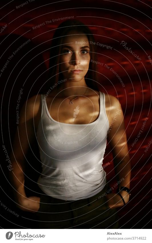 Portrait einer jungen Frau in Lichtstreifen von Jalousie vor roter Wand Licht und Schatten sportlich feminin Empathie Gefühle emotional Blick in die Kamera