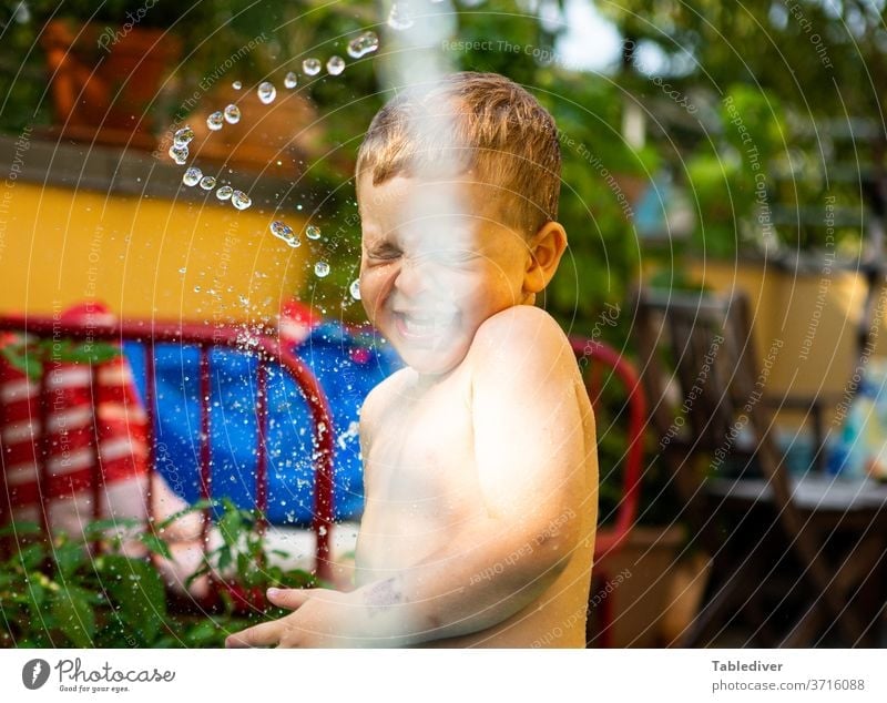 Junge wird auf der Terrasse mit Wasser bespritzt und lacht platschen spritzen Kind nackt Haut Garten Balkon Planschbecken Garten-Schleife Tropfen Wassertropfen