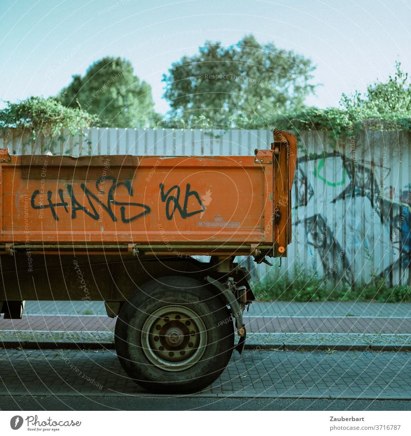 Ladefläche eines Lkw in Orange vor Wand aus Blech Lastkraftwagen Laster orange Räder Reifen Blechwand Zaun Grafitti Straße Pflaster Radweg Stand stehen