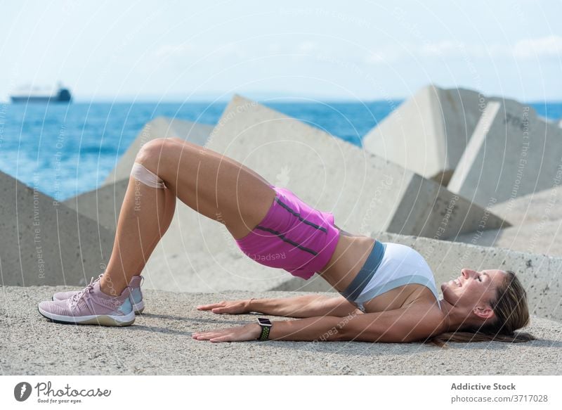 Schlanke Frau während des Hüfttrainings am Meer Brücke Übung Training Hüfte Pumpe Wellenbrecher widersetzen Band elastisch stark Körper Athlet Gesundheit