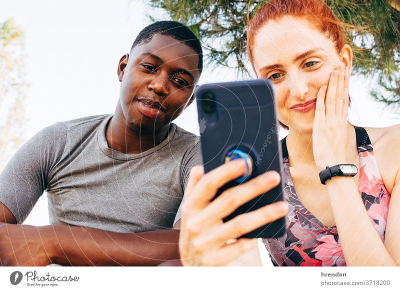 Freunde schauen auf das Smartphone, nachdem sie im Freien trainiert haben Freundschaft Gesunder Lebensstil Handy Frau Blick Fröhlichkeit junger Erwachsener