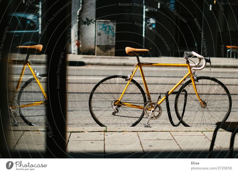 Gelbes vintage Rennrad steht abgeschlossen auf der Straße vor einem Geschäft Fahrradschloss gelb Fahrradfahren retro Sattel Ledersattel Sport Lifestyle trendy
