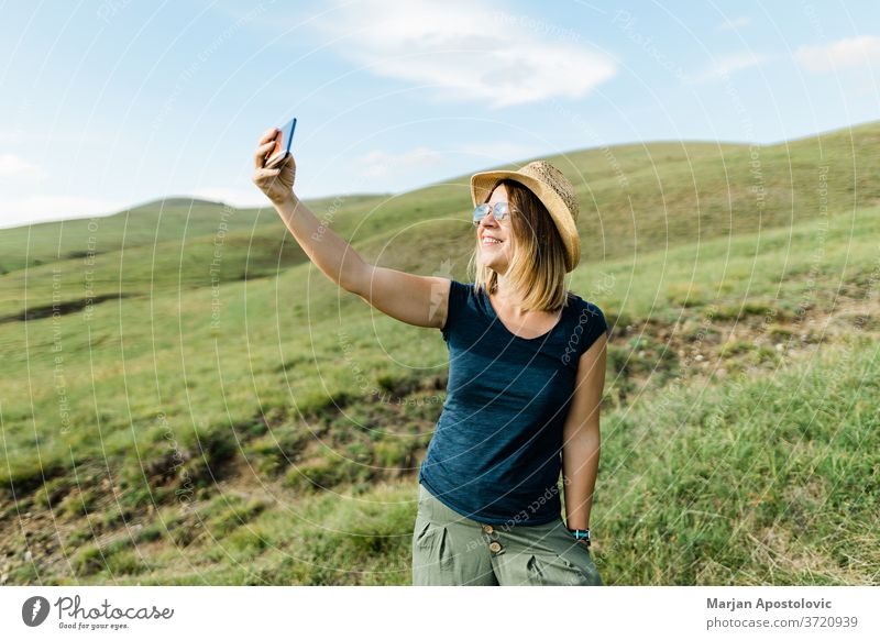 Junge Frau, die im Sommer auf einer Wiese am Hang ein Selfie macht Erwachsener Abenteuer schön Blog Blogger bloggend Fotokamera Kaukasier heiter Land niedlich