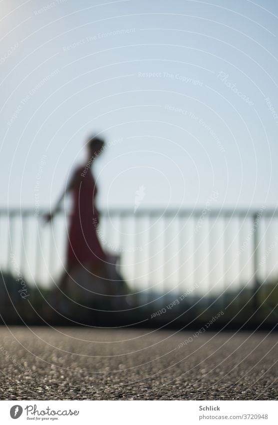 Junge Frau geht mit Tasche vor einem Geländer über Asphalt starke Unschärfe gehen Profil unscharf Himmel blau Kleid Sommer Gegenlicht Silhouette