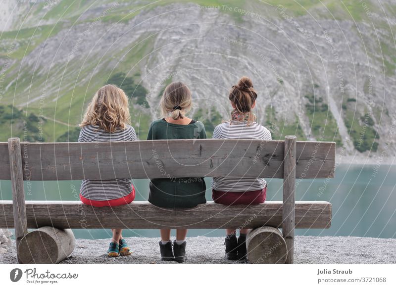 Drei Junge Frauen sitzen auf einer rustikalen Holzbank an einem Bergsee wandern Pause ausruhen Ruhe Berge u. Gebirge grau steinig alpin petrol See Gruppenfoto