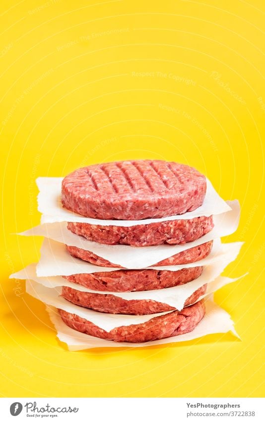 Burger-Pasteten auf dem Tisch gestapelt. Rohe Rinderfrikadellen isoliert auf gelbem Hintergrund. Barbecue grillen Rindfleisch Metzger Nahaufnahme Komfortnahrung