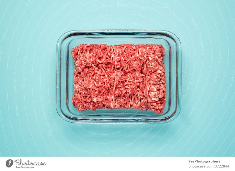 Rohes Rindfleisch in einem Lebensmittelbehälter aus Glas. Gemahlenes Fleisch in Glasschale, isoliert auf farbigem Hintergrund obere Ansicht blau