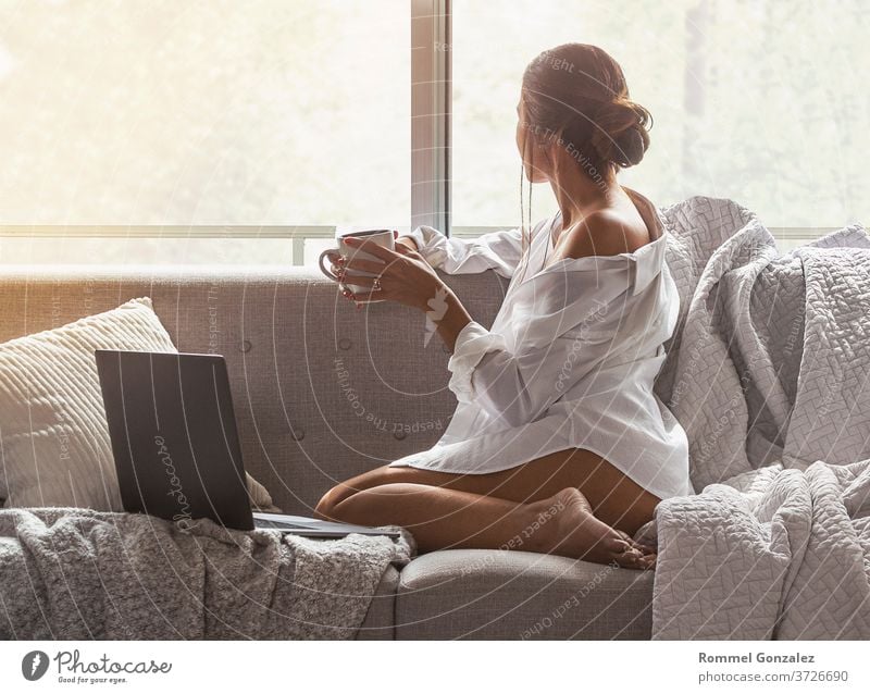 Schöne und sexy junge Frau, die einen Laptop benutzt, während sie auf dem Sofa sitzt Fenster einer Luxuswohnung. Stil blond Innenbereich Unschuld brünett