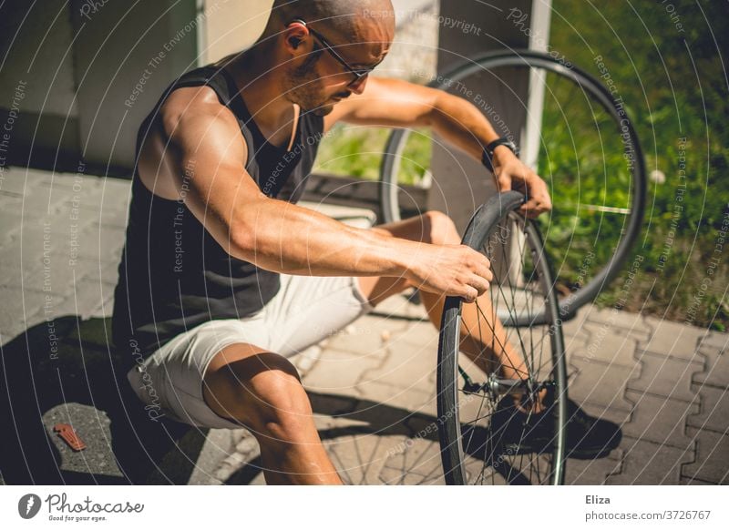 Ein Mann sitzt draußen in der Sonne und zieht einen Fahrradmantel auf das Laufrad seines Fahrrads, nachdem er den Schlauch geflickt hat reparieren Mantel