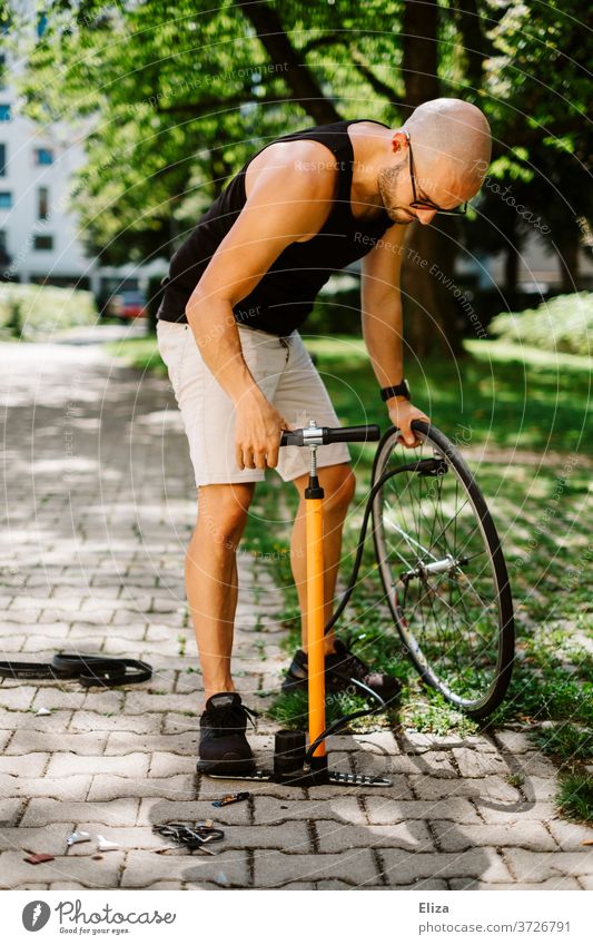 Ein Mann pumpt den Reifen seines Fahrrads mit einer Luftpumpe auf reifen aufpumpen draußen Sonne reparieren kurze Hose Glatze selber machen Rad sportlich