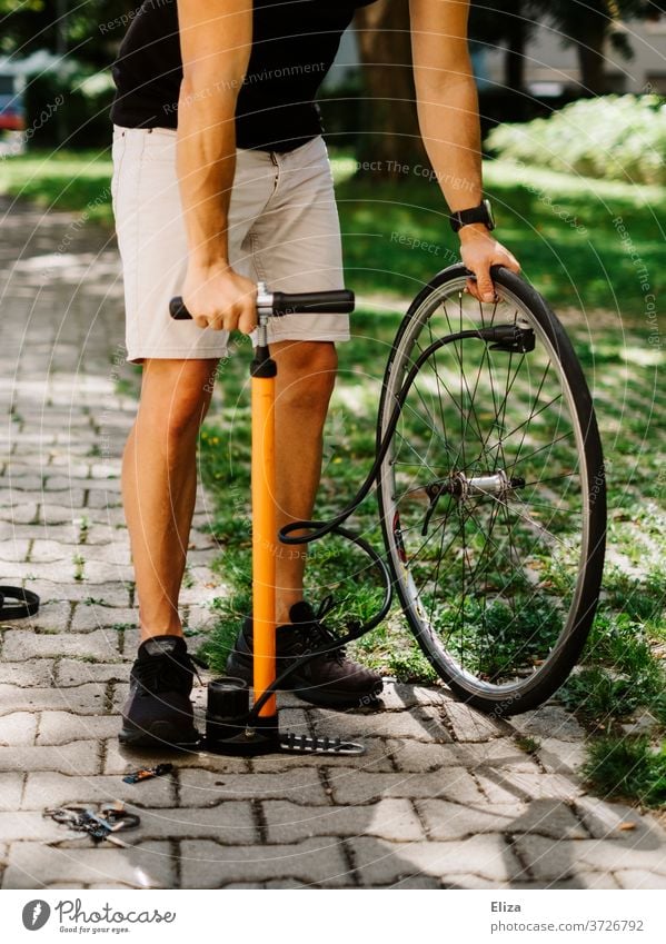 Ein Mann pumpt einen Fahrradreifen nach der Reparatur mit einer Luftpumpe auf Reifen aufpumpen Platten orange Sommer selber authentisch Rad Tag Sonne draußen