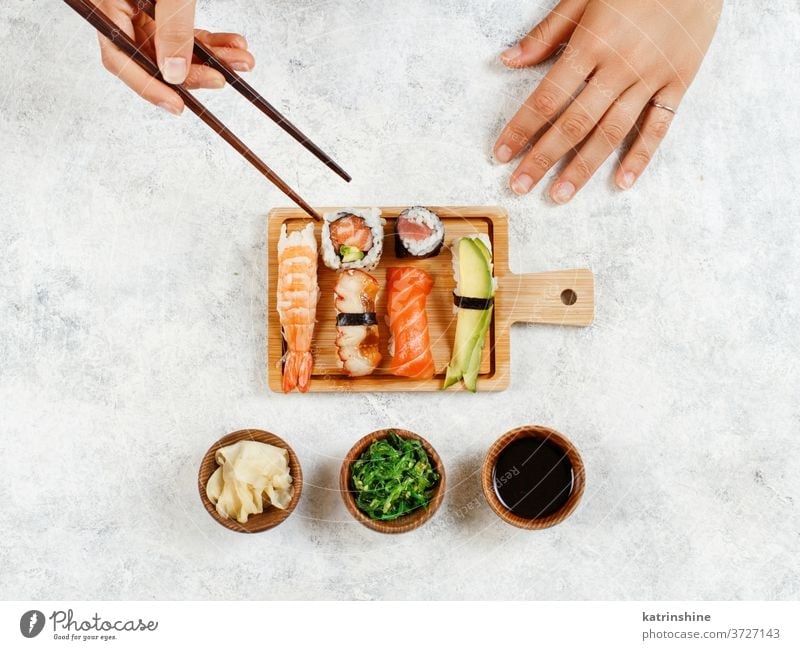 Draufsicht auf die Hand, die mit Stäbchen eine Rolle nimmt Sushi unter Essstäbchen verzehrfertig Essen Sashimi Brötchen Sushi-Bar Esszimmer Japanisch Kultur