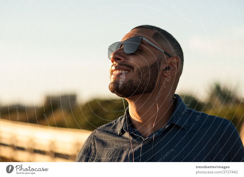 Lateinamerikaner, der über Kopfhörer Musik oder Motivationspodcasts hört und den Sonnenuntergang genießt Meditation Podcast Berghänge Urlaub Strand außerhalb