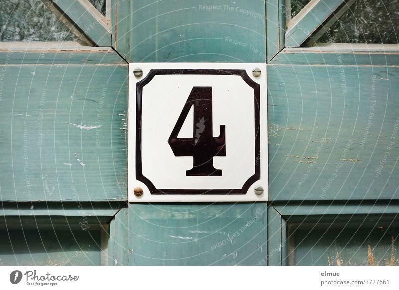 Die Zahl vier steht in schwarz und eingerahmt auf einem quadratischen Schild an der alten, blauen Holztür 4 Nummernschild Altbau Haustür Tür wohnen