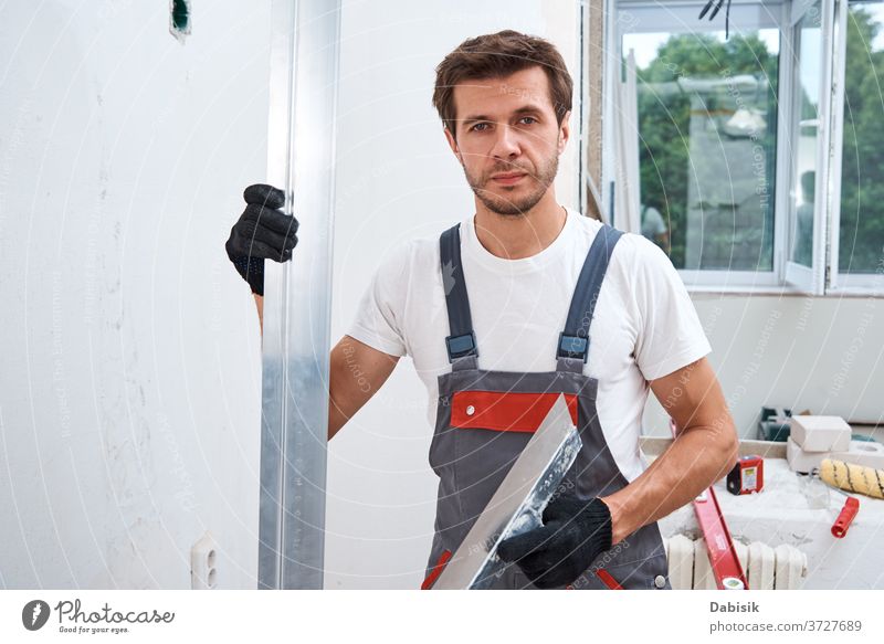 Renovierungskonzept. Männlicher Arbeiter verputzt eine Wand mit einem langen Spachtel verputzen Mann Werkzeug Stuck Industrie manuell Reparatur Konstruktion