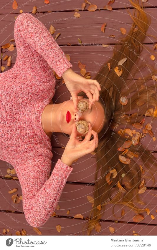 Wo ist der Herbst? Junge Frau, die auf einem Holzdeck liegt und ihre Augen mit riesigen Eicheln bedeckt. Spaß haben Model natürlich Gesicht Porträt Blatt