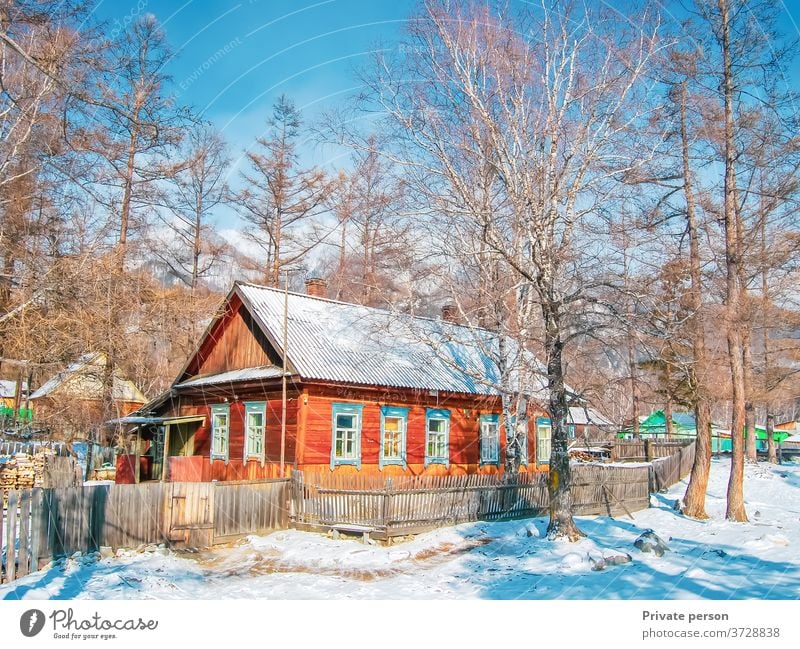 Malerisches Holzhaus im Wald an einem sonnigen Wintertag. Schnee, blauer Himmel, Berge im Hintergrund. Gesundes Lebenskonzept, ländliches Leben. Dorf weiß
