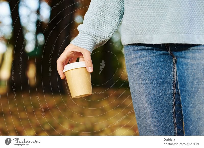 Frau hält Tasse Kaffee zum Mitnehmen im Herbstpark im Freien weg Tee trinken Einwegartikel Papier Hand gehen Sie heiß Morgen Latte Imbissbude Halt Beteiligung