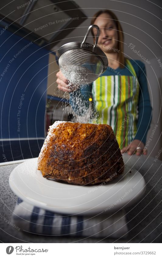 Frau mit einem Gugelhupf in einer Küche gugelhupf süß Dessert Essen Zucker lecker Kuchen Hintergrund Ernährung weiblich Gebäck hausgemacht bestreuen