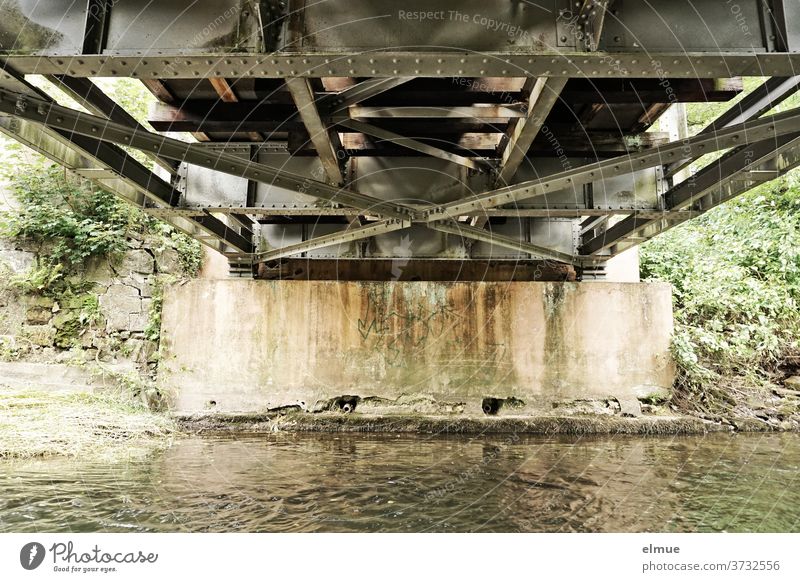 Blick auf die Unterseite einer kleinen Stahlbrücke, die einen Fluss überspannt Brücke Metall Eisenbahnbrücke Brückenpfeiler Brückenkonstruktion Niete Wasser