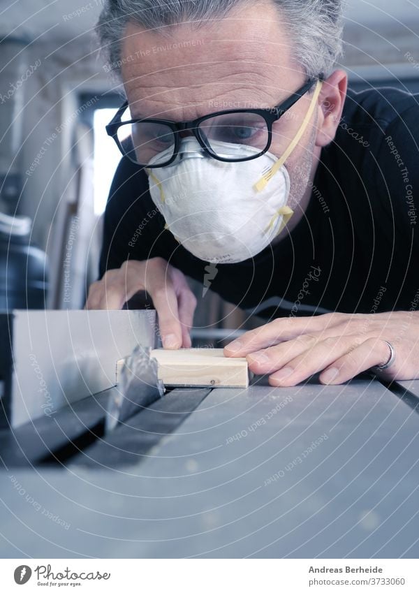 Mann mit Staubmaske und Schutzbrille bei der Arbeit an einer Kreissäge Werkzeuge Maschine Heimwerker Arbeiter Herstellung Aktivität schützend beruflich