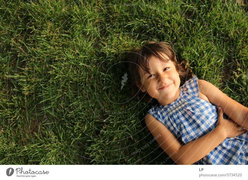 Mädchen lächelt in die auf dem Gras liegende Kamera Oberkörper Porträt Textfreiraum links Strukturen & Formen Muster abstrakt Außenaufnahme Gedeckte Farben