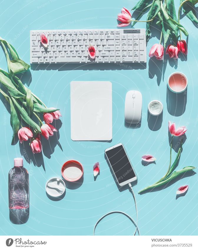 Frühjahrskonzept . Smartphone-Attrappe. PC-Tastatur, Tulpen und Naturkosmetikprodukte. Hellblauer Hintergrund. Lifestyle-Schönheitsblogging-Konzept. Flachlegen. Ansicht von oben