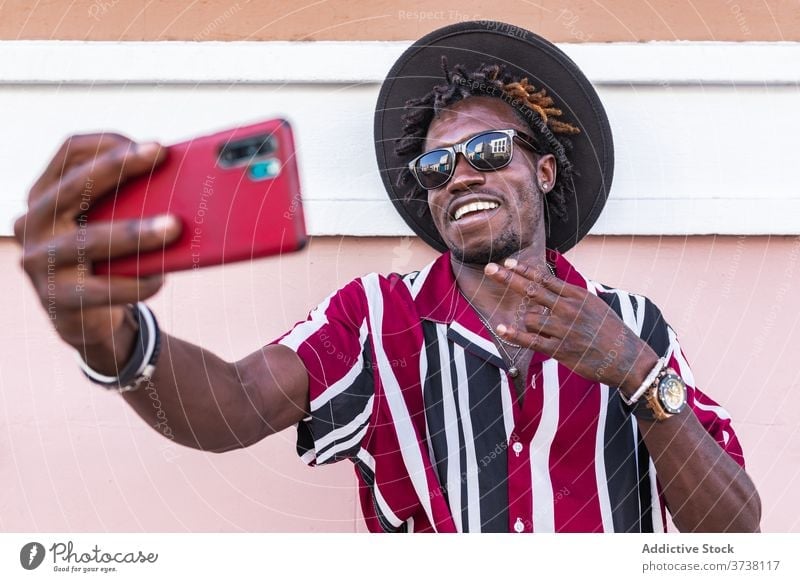 Fröhlich ethnischen Mann in stilvollem Outfit unter Selfie auf der Straße Stil Mode Smartphone heiter trendy flippig Hipster jung Sonnenbrille Streifen modern