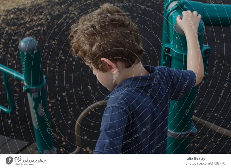Junge auf dem Schulhof Spielplatz Schule Spielen Kind Grundschule elementar blau grün lockig krause Haare Einsamkeit allein Pupille Dschungelturnhalle Park