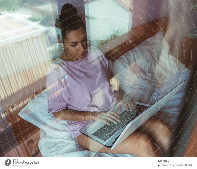 Junge Frau bei der Telearbeit, während sie einen Videogespräch am Laptop führt und auf dem Bett sitzt. Junge Studentin im Online-Unterricht. im Innenbereich