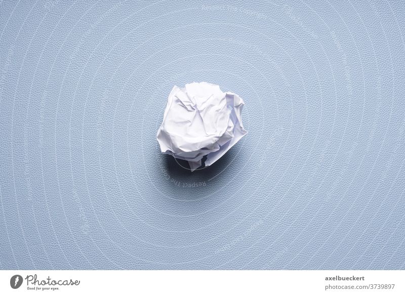 zerknüllte Papierkugel auf blauem Schreibtischunterlage Papierball Ball zerknülltes papier zerknittert verwerfen entsorgen Konzept scheitern Idee Müll