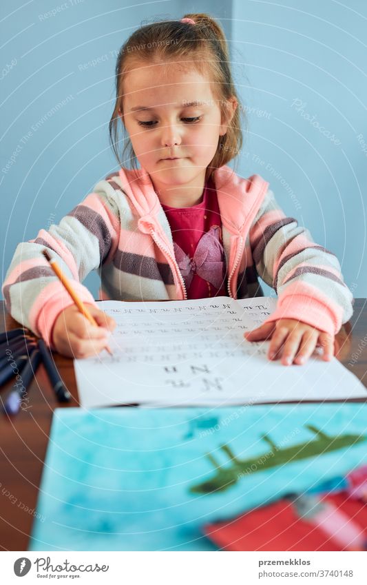 Kleines Mädchen im Vorschulalter, das in der Schule lernt, Briefe zu schreiben. Kleines Kind, das Briefe schreibt und eine Schularbeit schreibt. Konzept der Früherziehung