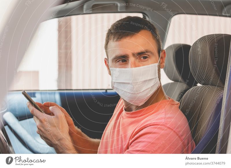 Ein junger Mann, der einen Mundschutz aus Stoff trägt, überprüft das Mobiltelefon im Auto Menschen schützend Virus Pflege Erwachsener Person Porträt Schutz