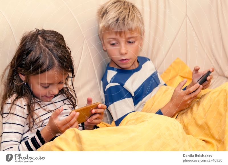 Kleines Mädchen und Junge spielen ein Spiel oder sehen sich etwas auf einem Smartphone an Cartoons Handy aussruhen Karikaturen anschauen Surfen im Netz