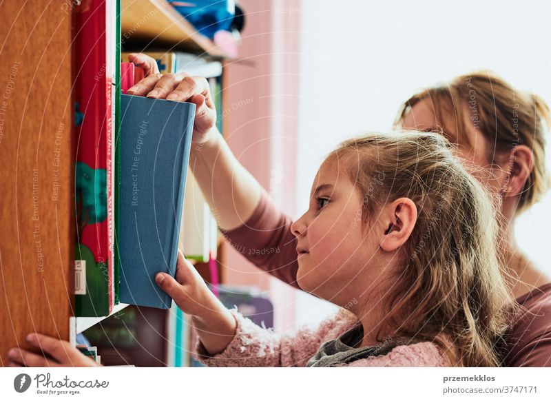 Kleines Mädchen im Vorschulalter wählt ein Buch zum Lesen Vorschulkind lesen auserwählend Bücherregal Bibliothek Bücherschrank Blick Bildung Fund Aussehen