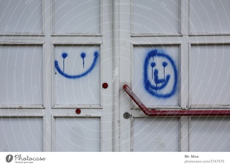 Smileys links und rechts Tür Eingang Eingangstür weiß blau Schmiererei Türgriff Lächeln Gute Laune geschlossen Griff Holztür alt Schloss Fröhlichkeit rund