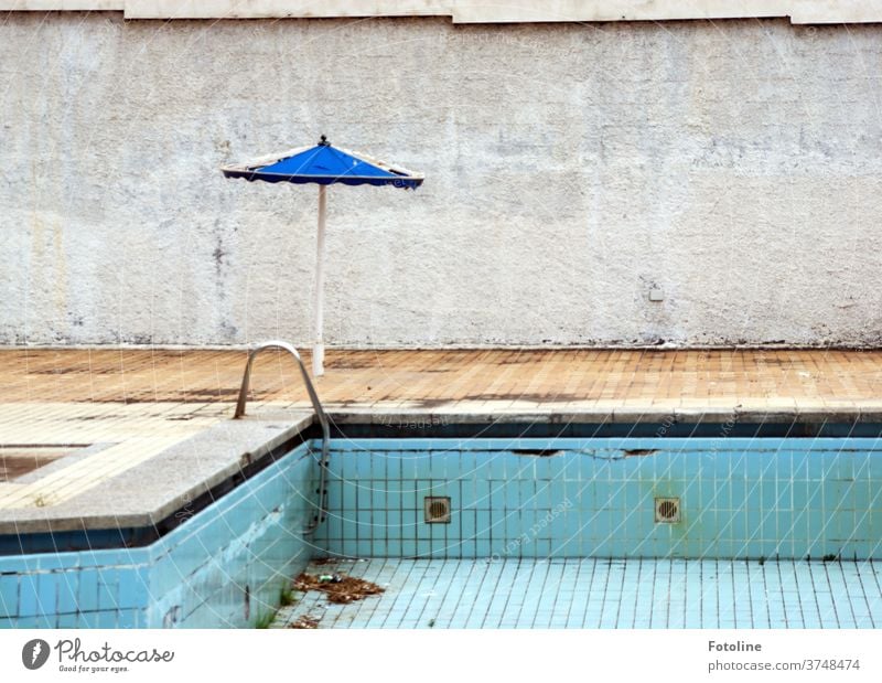 Hier schwimmt keiner mehr - oder ein runtergekommener Pool mit kaputtem Sonnenschirm an einer Betonmauer lost places Schwimmen & Baden alt Menschenleer Farbfoto