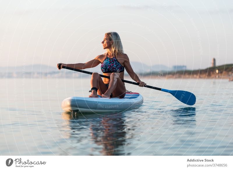 Frau übt auf Paddleboard bei Sonnenuntergang Paddelbrett Surfer Zusatzplatine Reihe MEER Training Surfbrett Sommer Holzplatte sportlich sitzen Windstille Wasser
