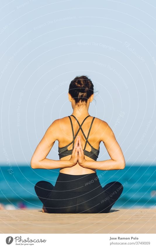junge Frau von hinten, die an einem sonnigen Tag vor dem Meer Yoga macht Rücken Meditation Gesundheit Sand Sitzen Menschen passen Erholung Sonnenschein ruhig